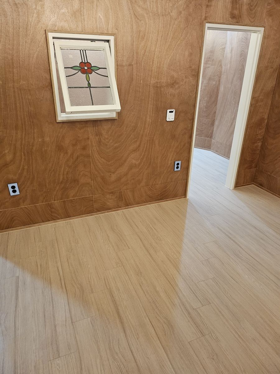 합판 마감 벽과 스테인드글라스 창이 있는 방. 비비드오크 강마루를 시공하고 문 너머 복도까지 이어진 모습.